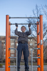 Teenager working out outdoors doing pull-ups on horizontal bar on the playground in the park