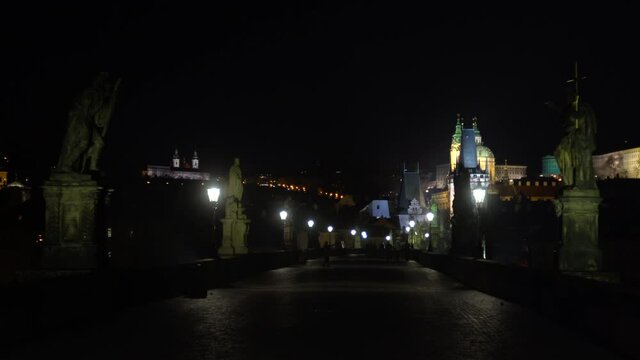 
street lights and statues on the stone Charles Bridge at night and silhouettes of walking people on the bridge at night in the center of Prague