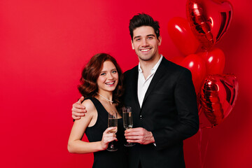 Happy man drinking champagne with wife on red background. Romantic couple expressing sincere emotions.
