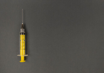 Yellow syringe on grey background. Simple flat lay with copy space.
