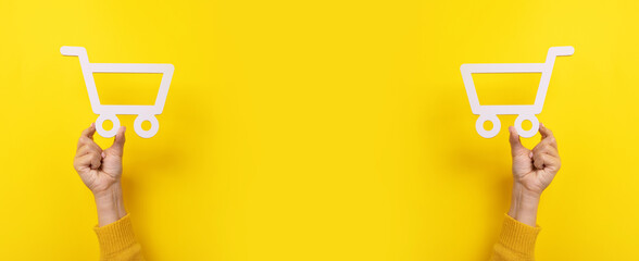 shopping cart symbol in hands over yellow background, panoramic image © alesmunt