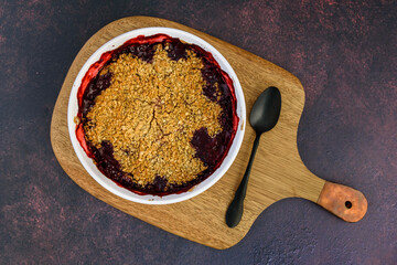 Fresh baked blueberry strawberry crisp baked in a white dish, sitting on a wood cutting board
