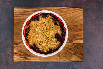 Fresh baked blueberry strawberry crisp baked in a white dish, sitting on a wood cutting board
