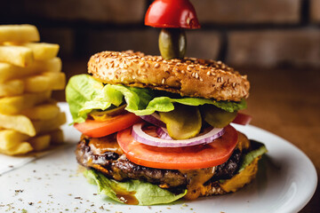 Burger with beef tomato onion and lettuce leaves on a plate with brick wall background - Burger with potato chips served at restaurant
