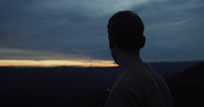 Close up view of the back of the white male at the summit of the mountain looking around in the dark towards the sunrise or sunset on Mount Batur in Bali, Indonesia
