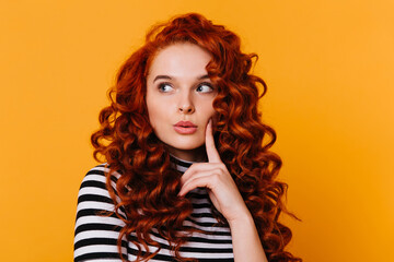 Close-up shot of attractive girl in striped T-shirt looking pensively to side against orange background