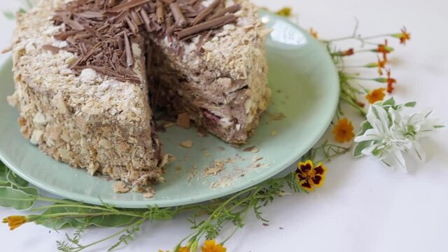 cake with nuts and chocolate, decorated with chocolate chips. cake stands on a plate and flowers. cut cake on a plate