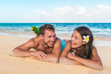 Beach couple having fun on honeymoon vacation holiday tanning lying down on Caribbean sand laughing...