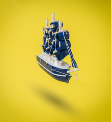 A blue ship with sails on a bright yellow background.