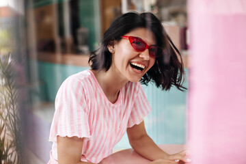 Laughing dark-haired woman posing in sunglasses. Outdoor shot of excited tanned girl expressing positive emotions.