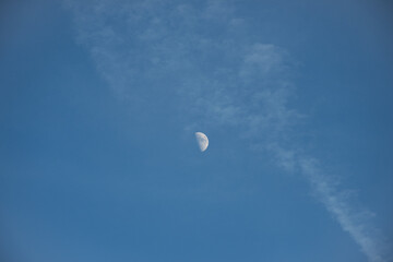 A half moon seen in a blue sky with a few clouds during daytime