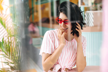 Selective focus of playful european girl in pink sunglasses. Outdoor shot of cheerful brunette lady in pink t-shirt.
