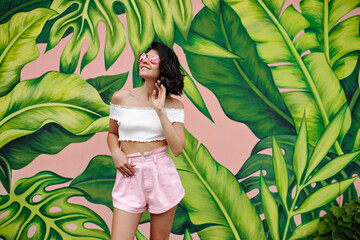 Dreamy girl in summer attire looking up with smile. Lovable slim woman posing near graffiti.