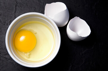 Raw Egg in a White Bowl with Shells on Dark Background