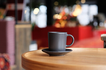 A small black coffee cup on a saucer on a wooden table. Coffee in a cafe on the background of blurred background