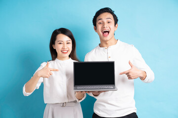 Portrait of happy young couple using laptop on blue background