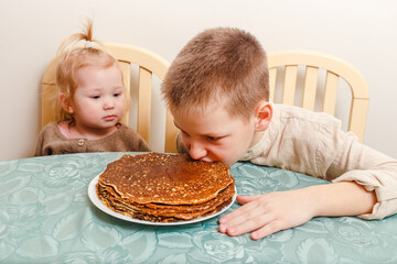 two children sit at a table with plate of large pancakes. Breakfast. Children eat. Brother and sister at home