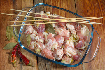 Boneless pork steak, sliced and marinated with onions, meat in a glass bowl, chili pepper, marinades on a wooden table.Cooking shish kebab.Selective focus.