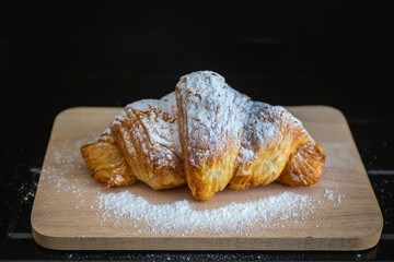 Croissant on a wooden plate with icing sugar and almonds on a black background. Select focus
