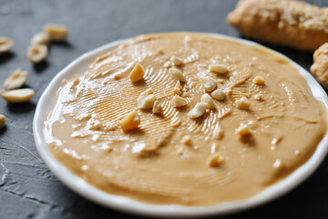 peanut butter on a plate with salted peanuts. paleo diet and keto diet food. traditional ingredient for tasty breakfast. dark background. fats source. selective focus.