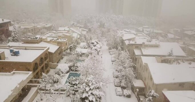 View of Tehran city landscape in Iran during the heavy snow fall.
Building roof, Houses, pools, pine trees and foliage covered by white snow in a very cold freezing day. aerial view along a street.