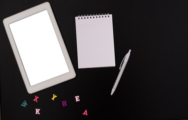 Online courses. The study of the English language. A tablet with a copy of the space, a blank notepad, a pen, letters on a black background. Mock up