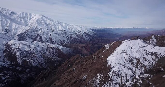 landscape of mountain covered by snow in a wide view cloudy sky visible in horizon. rural road links the villages in Alamut valley highlands in early winter in morning.