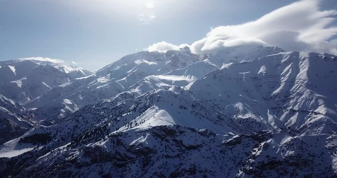 Fly over snow covered mountain and highland villages in Alamut valley in Iran sunny day with plenty of sunshine in the blue sky and juniper trees in the scenic landscape are visible in outdoor trip