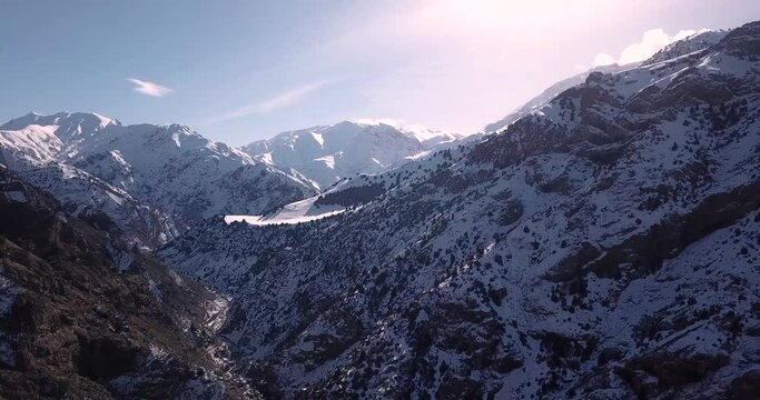 fly over an snow covered valley with a rural road to village. Persian Juniper trees visible in beautiful scenic cinematic winter landscape in Alamut in Iran. mountains full of snow in a cold sunny day