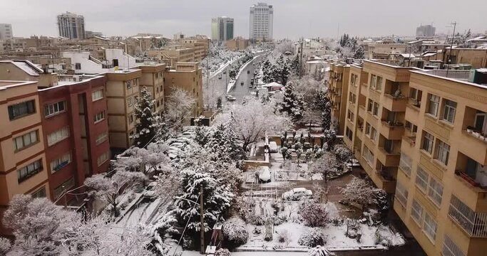 beautiful cityscape of Tehran in Iran. buildings with yard and pool have many of tree in yard covered by snow. aerial shot Birdseye view during snow fall and big towers in background landscape.