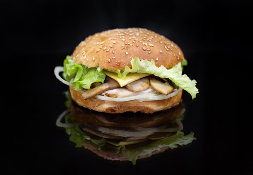 Hamburger close-up on a black background. Fast food and junk food. Burger with chicken and mushrooms