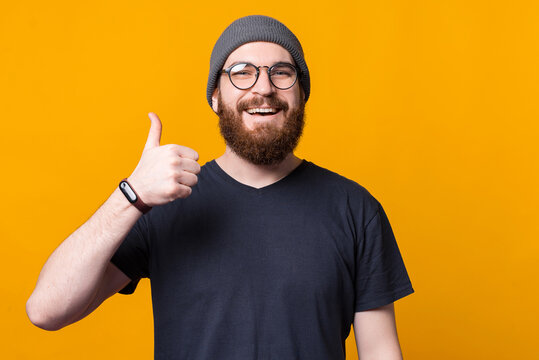 Nice picture of a young bearded hipster showing a thumb up smiling at the camera .
