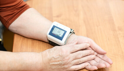 A close-up of an elderly woman's hand. A woman reduces blood pressure with a tonometer on her wrist.