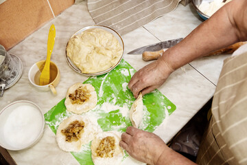 The concept of baking at home. View from above on the work surface with dough and hands of an elderly woman. A woman makes pies with stuffing.