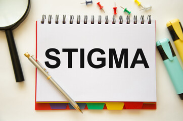 the word stigma is written on a notebook and a white background with a half-glass of colored pencils