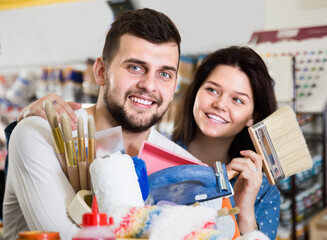 admiring loving couple demonstrating tools for house renovating in paint supplies store