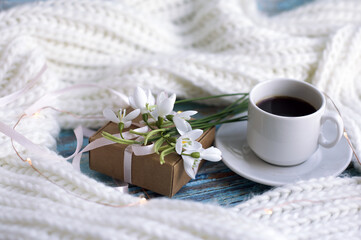 Obraz na płótnie Canvas a cup of coffee, knitted scarf, snowdrops. card for March 8.