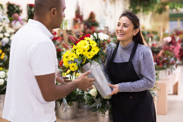 Fototapeta premium Experienced woman florist helping male client to choose flowers in flower shop