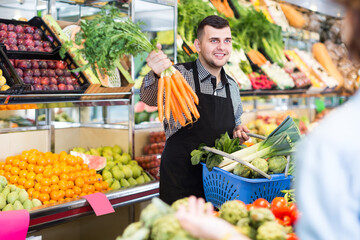 happy male shopping assistant helping customer to buy fresh fruit and vegetables in grocery shop