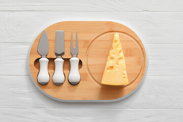 Piece of tasty cheese and knives on wooden background