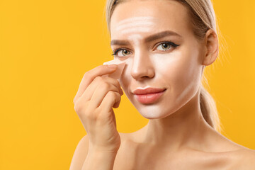 Beautiful young woman applying contouring makeup against color background