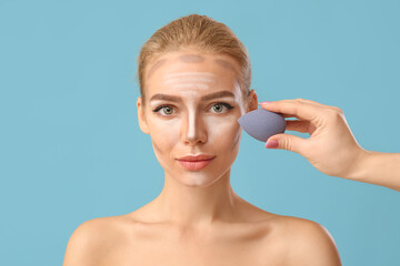 Cosmetologist applying contouring makeup on woman's face against color background