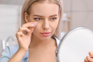 Beautiful young woman with sponge applying makeup at home