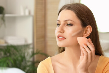 Beautiful young woman applying contouring makeup at home