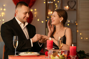 Young man putting ring on finger of his fiancee after marriage proposal on Valentine's Day at home