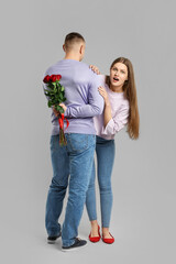 Young couple with flowers on grey background. Valentine's Day celebration