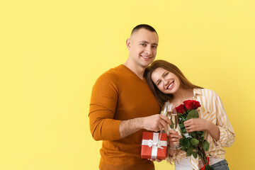 Young couple with glasses of champagne, gift and flowers on color background. Valentine's Day celebration