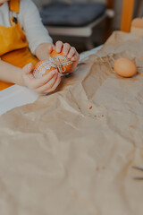 Baby girl decorating easter eggs on white table. Kid decorating eggs with kraft paper, lace and rope. Child holds easter eggs in hands.