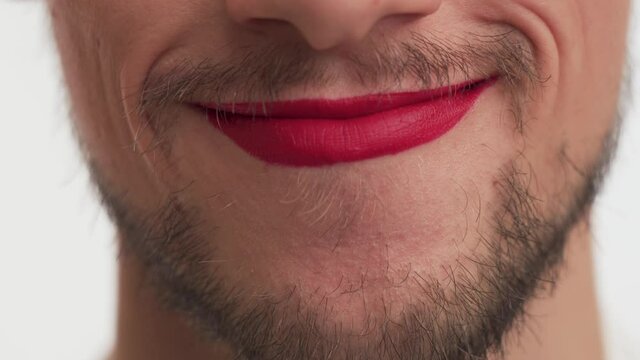 Single young happy effeminate Caucasian brunette bearded man with moustache, painted lips by red lipstick smiles many times, repeat. Close up mouth of pretty transvestite male on white background.