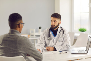 Young man consulting medical specialist at the clinic. Professional doctor talking to patient, discussing treatment methods, explaining how to maintain good health and prescribing effective medication